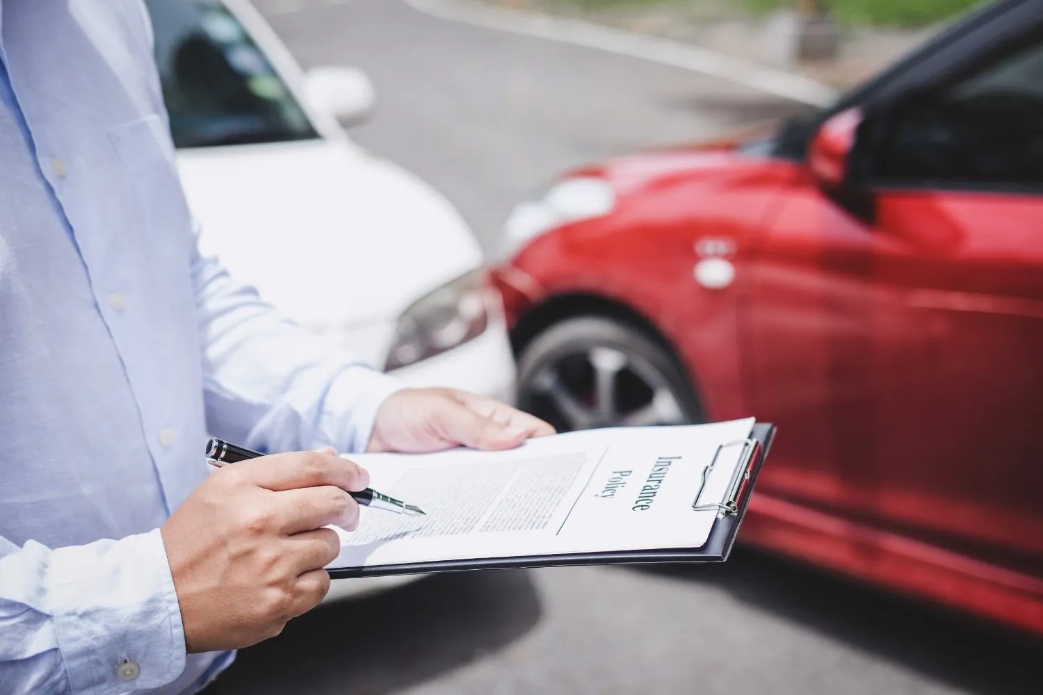 Person filling in an insurance policy form beside two cars after a bump